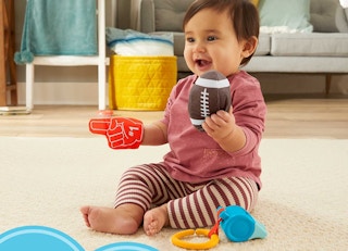 A baby on the floor playing with football-themed toys