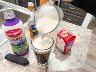 a person using milk, syrup and cream with electric frothier to create cold foam for iced coffee