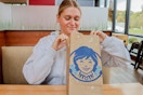 a person sitting at a table in Wendy's while holding a Wendy's to-go bag.
