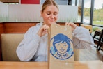 a person sitting at a table in Wendy's while holding a Wendy's to-go bag.