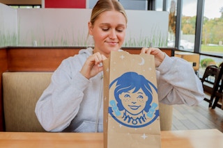a person sitting at a table in Wendy's while holding a Wendy's to-go bag.