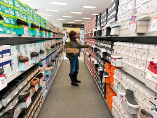 A woman holding a shoe box while looking at shoes on display inside Shoe Carnival.