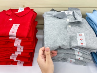 A person's hand taking a children's school uniform polo shirt from a shelf at Old Navy.