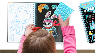 a kid playing with a foil crafting kit in a notebook