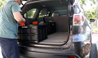 A man organizing items into CleverMade storage bins in the back of his car.