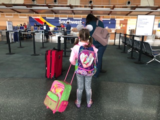 A little girl stands in line with luggage to go to Disneyland.