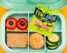 a kid's lunch container with food and a pack of fruit gummies inside