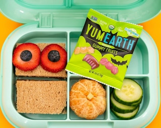 a kid's lunch container with food and a pack of fruit gummies inside