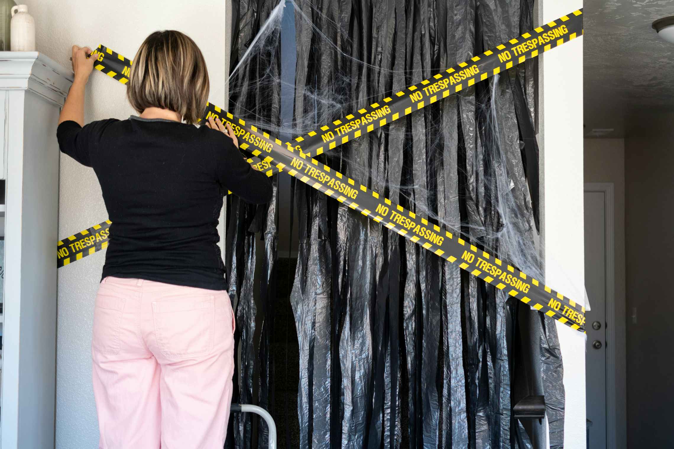 A woman hanging do not enter caution tape over a doorway covered with cut garbage bags.