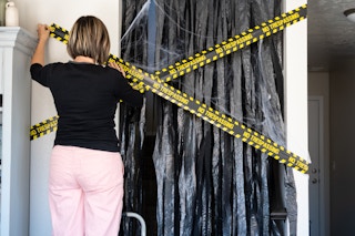 A woman hanging do not enter caution tape over a doorway covered with cut garbage bags.