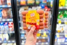 hand holding two packages of oscar mayer wieners in front of store coolers