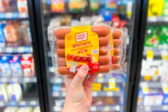 hand holding two packages of oscar mayer wieners in front of store coolers