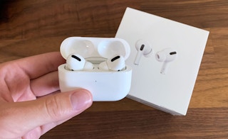 A person's hand holding Apple AirPods Pro With Charging Case above its box on a table.