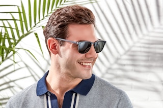 Male model wearing a pair of Foster Grand sunglasses with palm leaves behind him