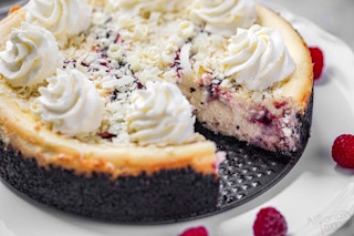 A close up of a white chocolate raspberry cheesecake with a slice taken out.