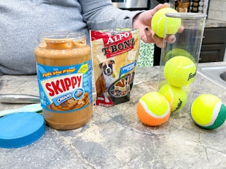 a person holding a tennis ball next to dog treats and peanut butter