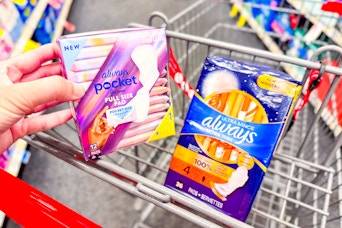 person holding a package of always pocket pads over a cart with always maxi pads in it