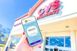hand holding a smartphone displaying a kcl coupon barcode in front of a cvs store