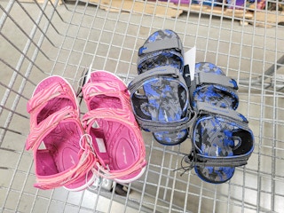 2 pairs of kids sandals in a cart, one is pink one is blue & black