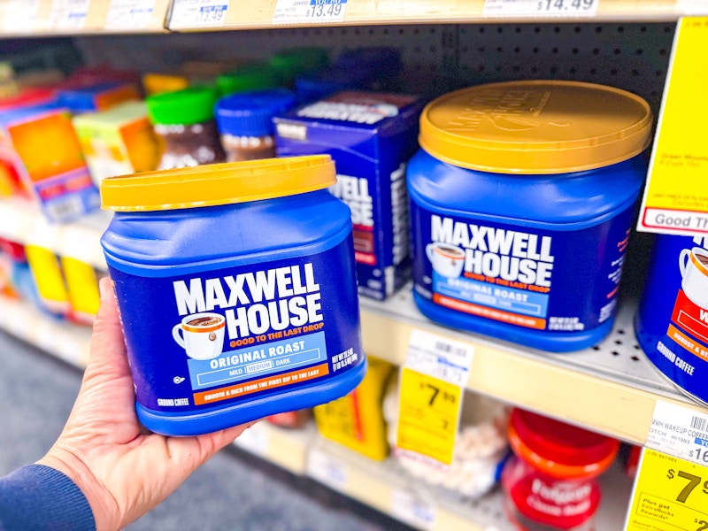 person holding a container of maxwell house coffee by a shelf of coffee