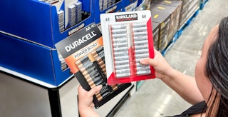 Person holding packs of Duracell batteries and Kirkland batteries.
