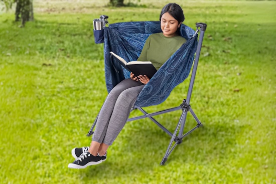 Lifestyle image of a girl sitting in the Ozark Trail Portable Hammock Camping Chair in a field of grass