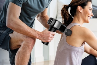 person using massage gun on back