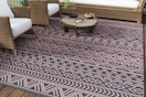 B0DHZDP681 Pink and grey outdoor rug on a deck with some woven rattan furniture with white cushions
