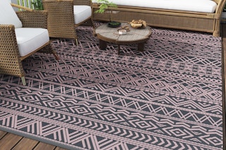 B0DHZDP681 Pink and grey outdoor rug on a deck with some woven rattan furniture with white cushions