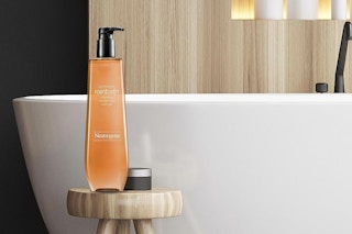 A 32-ounce bottle of Neutrogena Rainbath Shower Gel sits on a stool next to a bathtub.