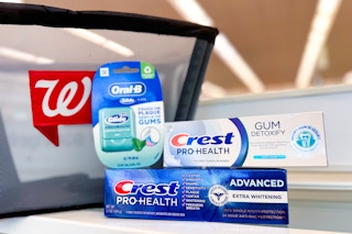 two crest toothpastes and oral-b floss on store counter in front of walgreens shopping basket