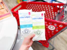 hand holding 2 packs of waterwipes in front a parked target cart
