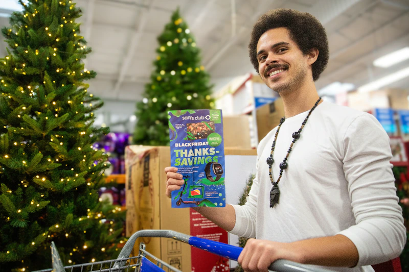 a person stand by a cart holding a sams club black friday book