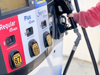 A person's hand reaching to take the nozzle from a gas pump with the fuel option buttons in the foreground.