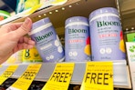 person grabbing a bottle of bloom supplements off a shelf with buy one get one free tags