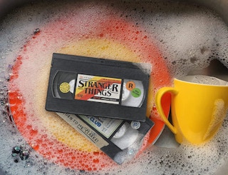Stranger Things VHS sponges in a sink with soapy water and dishes