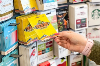 A person reaching to take a gift card from a display of gift cards.