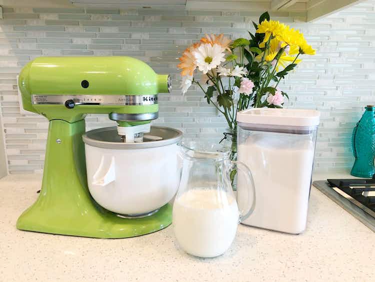 A kitchenaid ice cream maker with cream and sugar on the countertop.