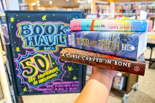 someone with a stack of books in had in front of the Book Haul sale sign at Barnes & Noble