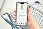 hand holding smartphone over shopping cart with kcl app and 1-clip coupon deal