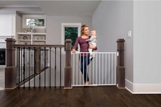 woman opening a top of the stairs baby gate holding a baby