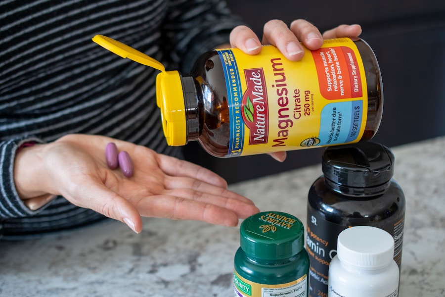 A person pouring two vitamins from a bottle into the palm of their hand