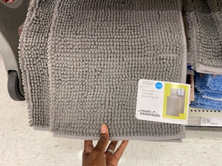 A person's hand taking a 2-pack of everyday chenille bath rugs from a Target shelf