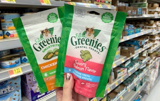a hand holding two bags of cat treats in a store aisle