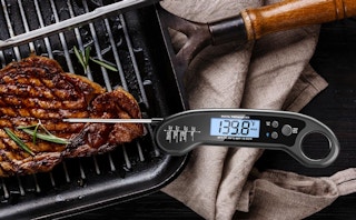a meat thermometer on a steak on a grill