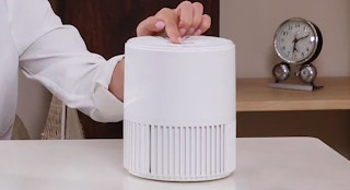 person pressing a button on the top of a compact air purifier