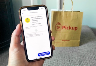 hand holding a smartphone with walgreens pickup bag in background