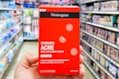 a hand holding a red pack of pimple patches in a store aisle