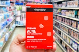 a hand holding a red pack of pimple patches in a store aisle