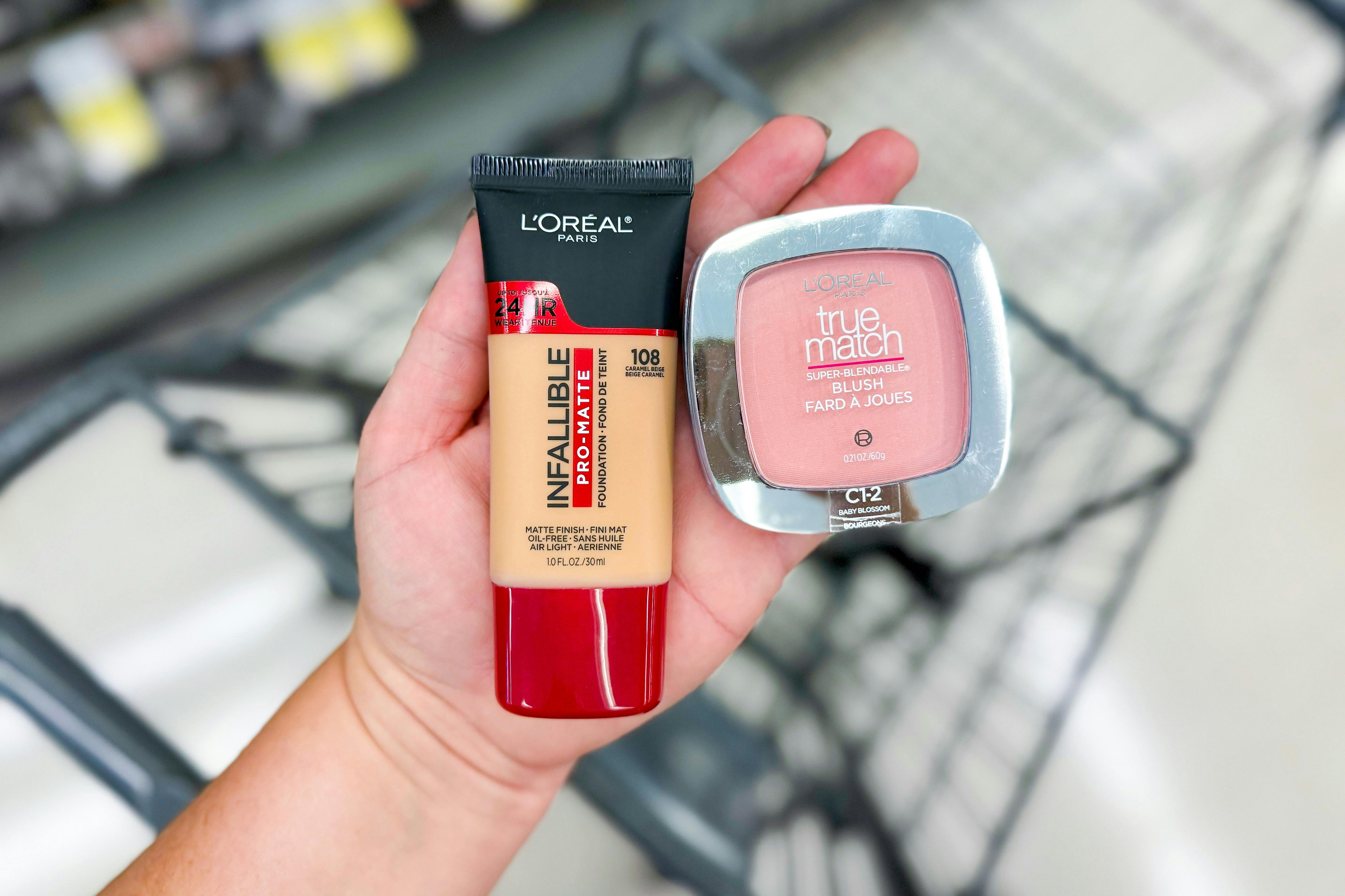 person holding maybelline foundation and blush over a cart